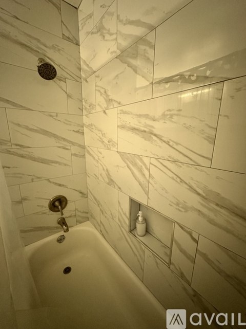 A bathroom with a marble tile wall and a white bathtub.