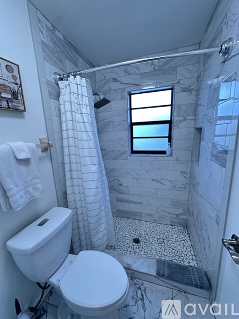 A bathroom with a toilet, a shower with a glass door, and a window.