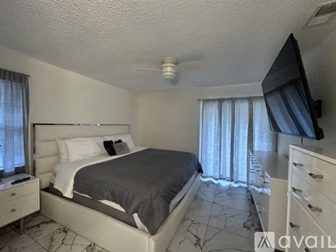 A bedroom with a large bed, a ceiling fan, and a flat-screen TV mounted on the wall.