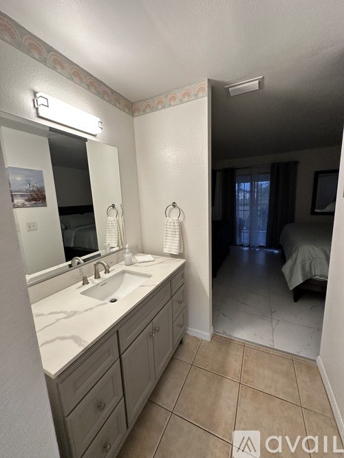 A bathroom with a sink, mirror, and a bedroom in the background.