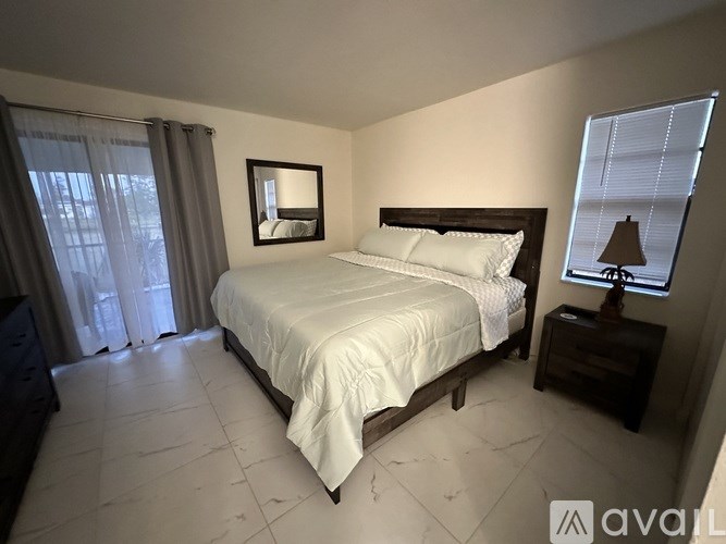 A bedroom with a large bed, a nightstand with a lamp, and a window with curtains.