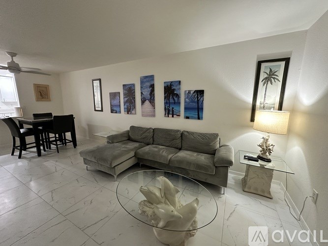 A living room with a grey couch, a glass coffee table, and a wall with framed pictures.
