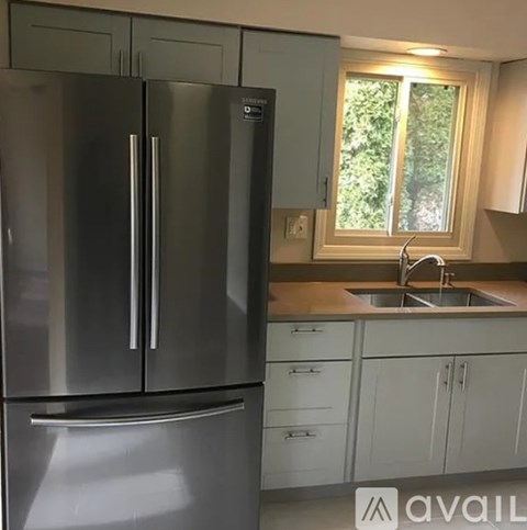 A stainless steel refrigerator stands in a kitchen with light wood cabinets.