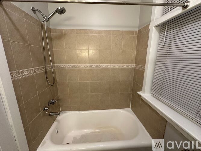 A bathroom with a beige tiled shower area and a white bathtub.