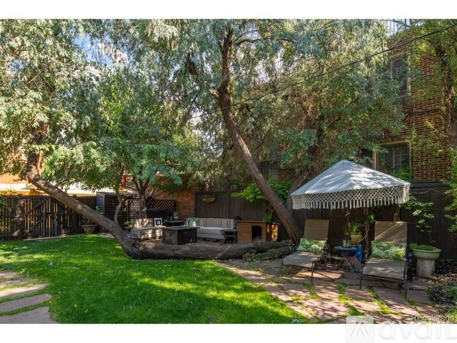 A backyard with a white canopy and a tree leaning over a picnic table.