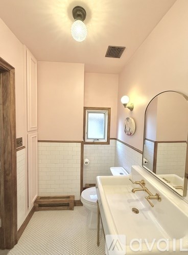 A bathroom with a toilet, sink, mirror, and a window.