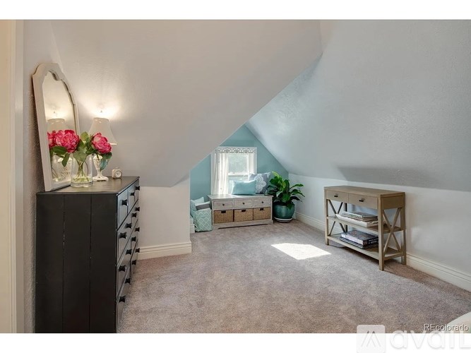 A room with a large mirror, a dresser, a window with a blue curtain, a potted plant, and a wooden shelf.