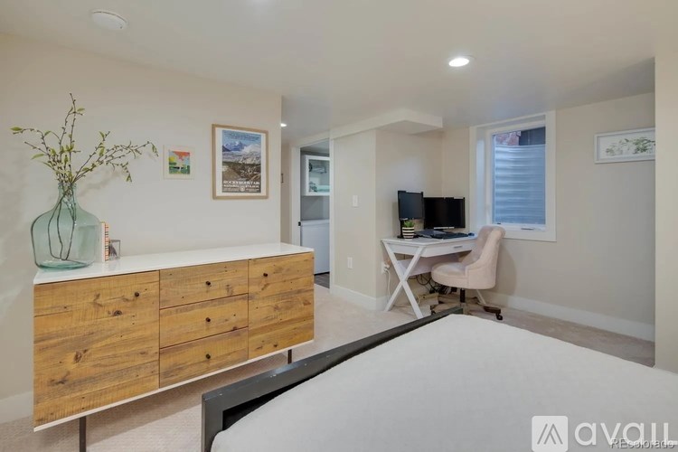 A room with a bed, desk, and a vase on top of a wooden cabinet.