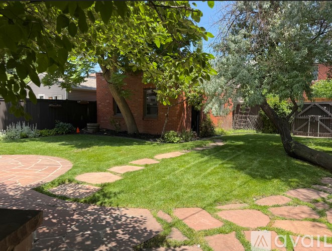 A backyard with a circular brick patio and a tree.