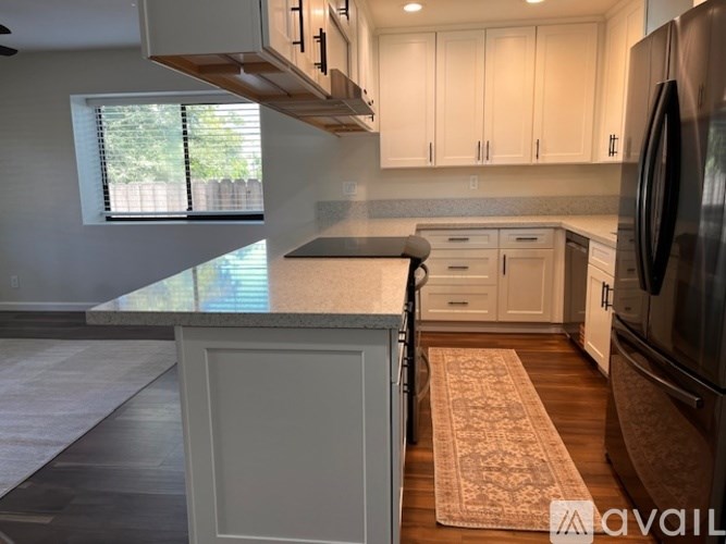 A kitchen with a refrigerator, cabinets, and a rug on the floor.