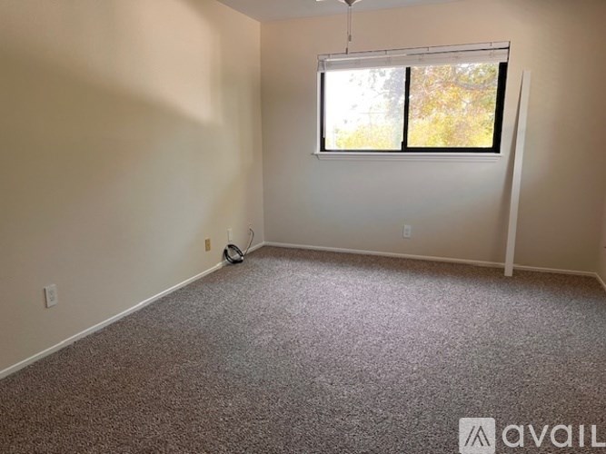A room with a carpeted floor, a window with blinds, and a fan on the wall.
