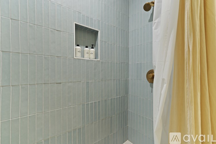 A bathroom with blue tiles and a white shelf with two bottles on it.