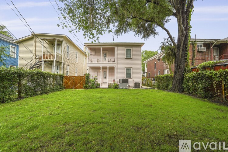 A grassy area with a tree and a house with a balcony in the background.