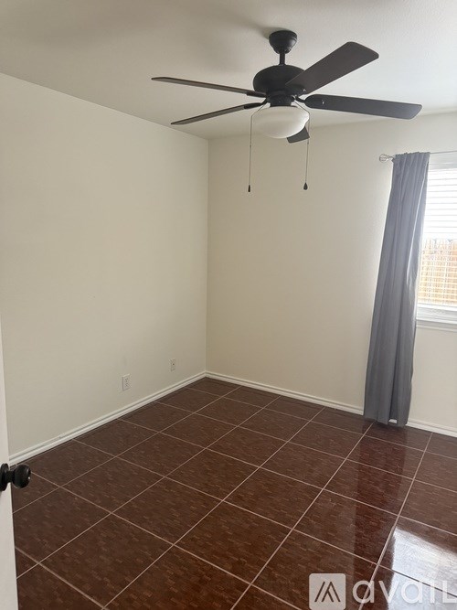 A room with a ceiling fan and brown tiled flooring.