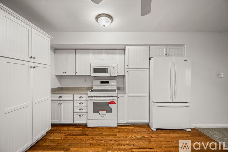 A kitchen with white cabinets and appliances, a wooden floor, and a ceiling fan.