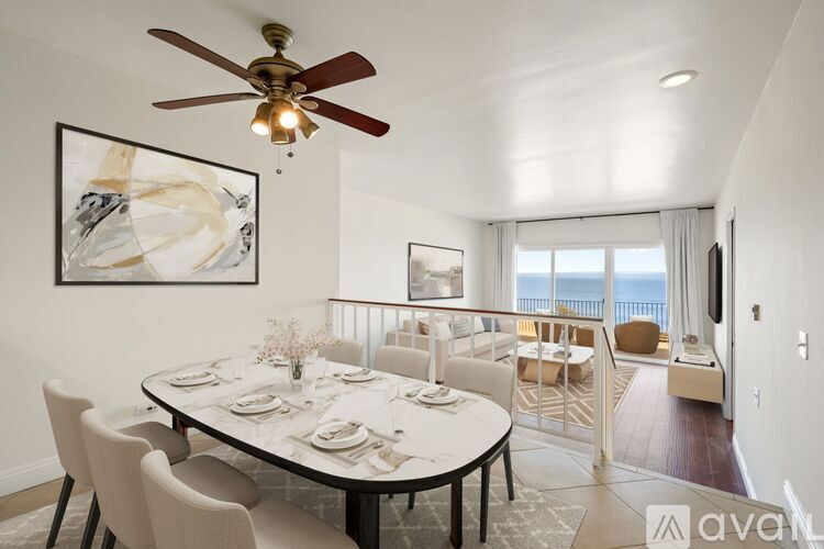 A dining room with a table set for six and a balcony with a view of the ocean.