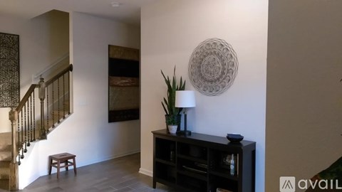 A living room with a staircase, a table with a plant and a lamp, and a wall hanging.