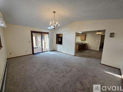 A spacious living room with a grey carpet and a chandelier hanging from the ceiling.