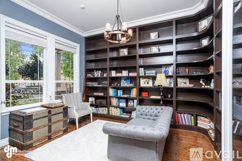 A living room with a grey sofa, a white chair, a bookshelf filled with books and a chandelier hanging from the ceiling.