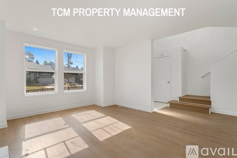 A room with wooden flooring and white walls, with a window showing a view of a house and trees.