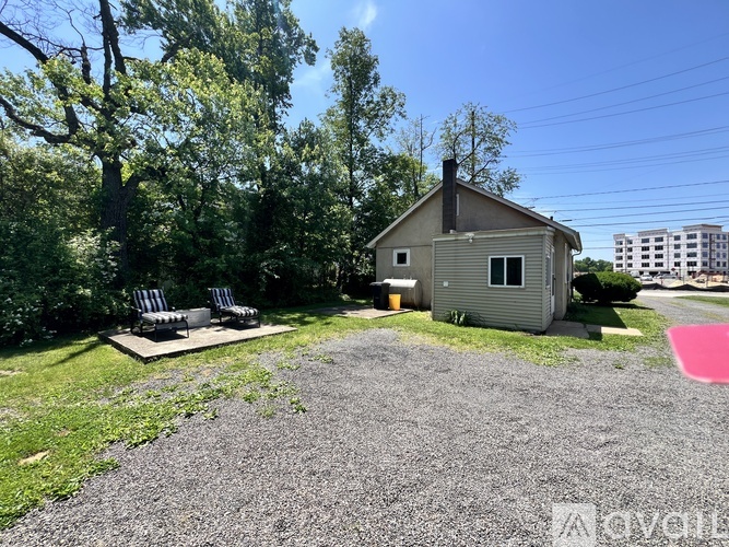 A small house with a grey roof and a gravel driveway in front of it.