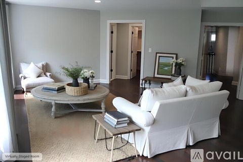 A living room with a white couch, a round table with a plant on it, and a painting on the wall.