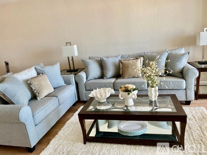 A living room with a grey couch, a glass coffee table, and a white rug.