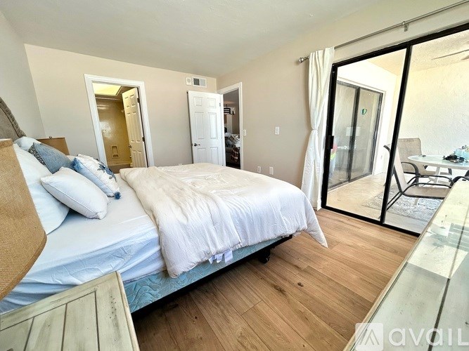 A bedroom with a large bed and a sliding glass door leading to a balcony.