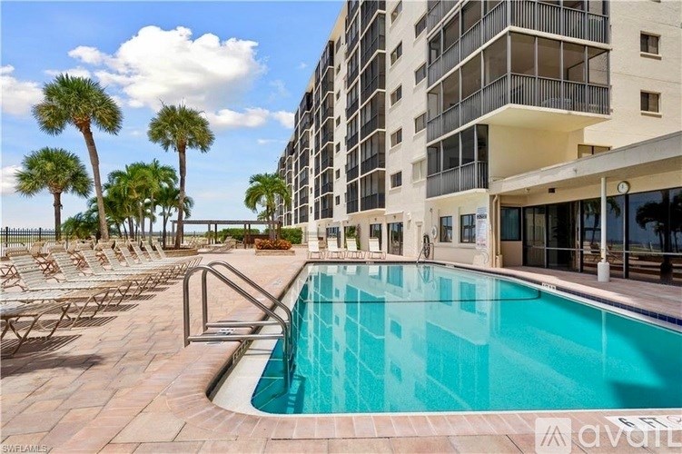 A large swimming pool is surrounded by a patio with chairs and palm trees.