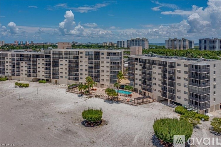 A large sandy area with a few trees and bushes in front of apartment buildings.