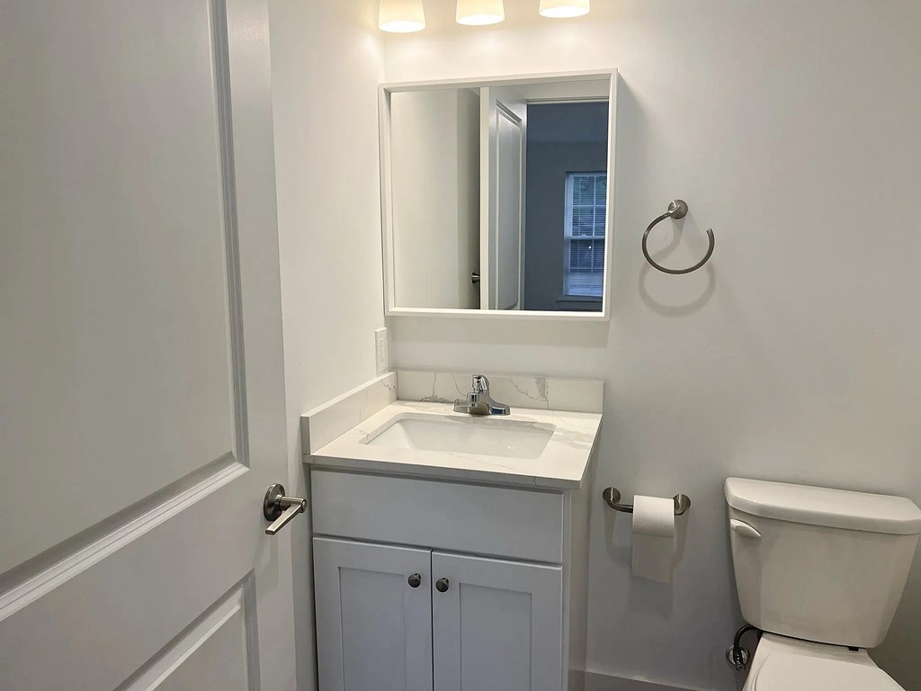 A white bathroom with a toilet, sink, and mirror.