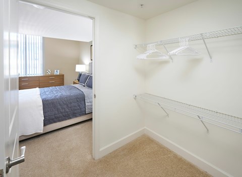 A bedroom with a bed, nightstand, and a closet with hangers.