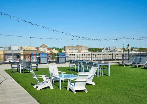 A patio with white chairs and a table is set up on a grassy area.