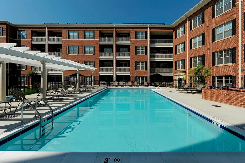 A large swimming pool in front of a brick building with lounge chairs and umbrellas.