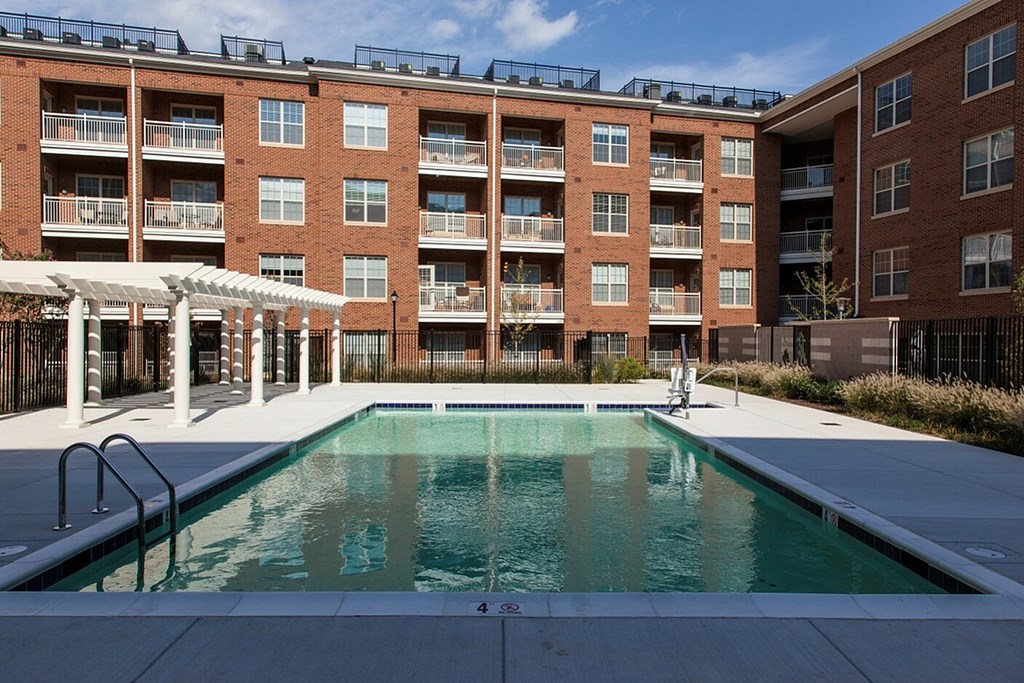 A swimming pool in front of a red brick building with a white pergola.