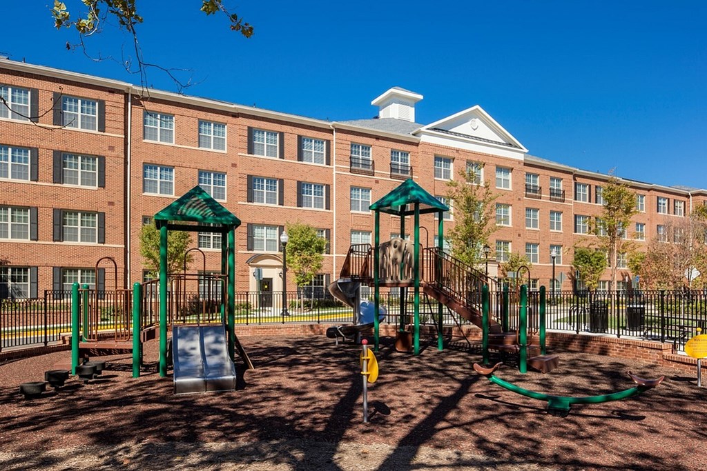 A playground with a green canopy and a yellow slide in front of a brick building.