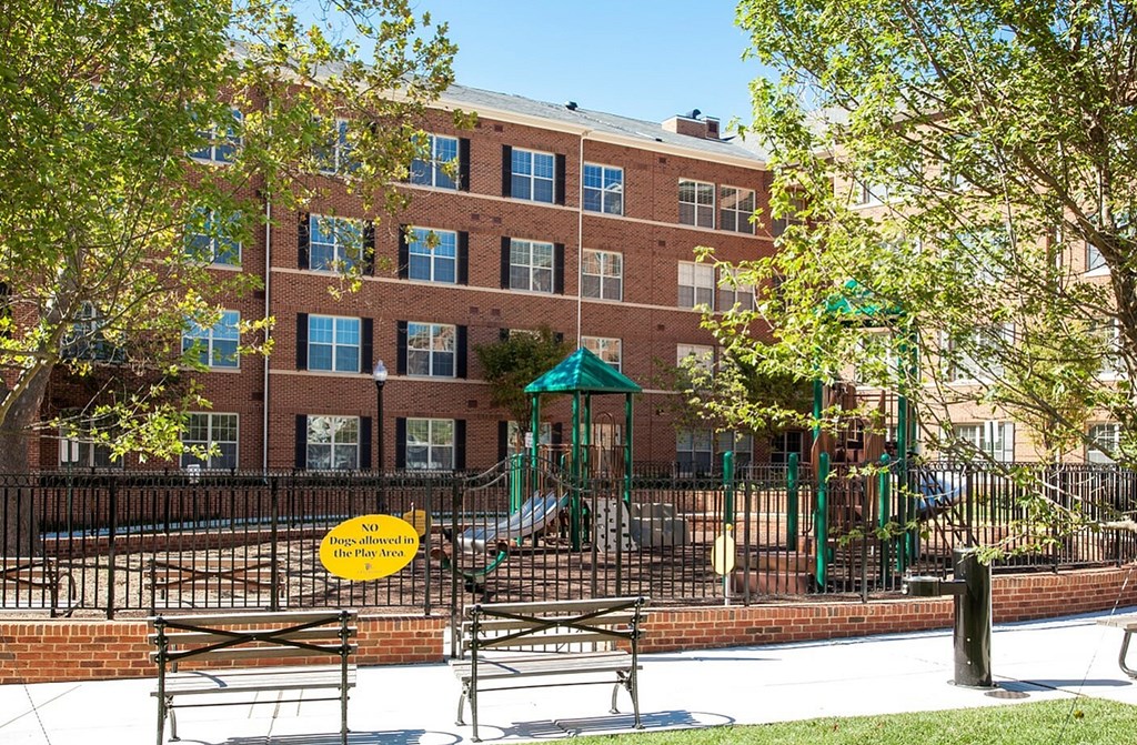 A playground with a sign that says "No Play Zone" is in front of a brick building.