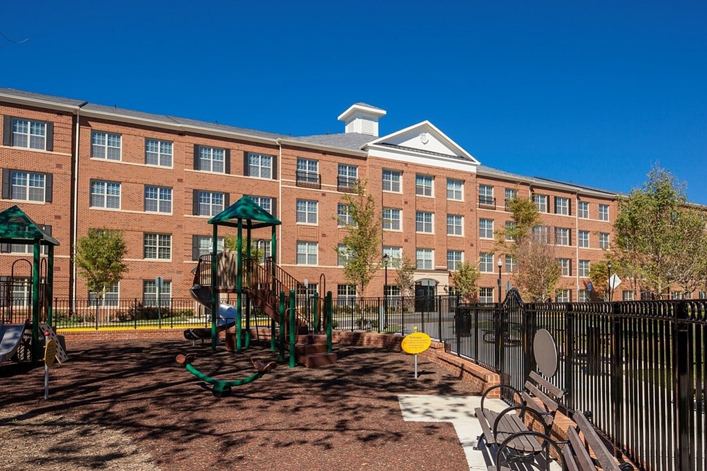 A playground with a swing set and a slide in front of a brick building.