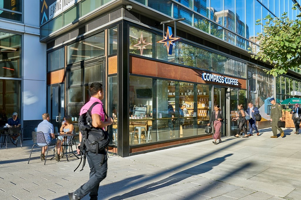 A man with a pink backpack is walking past a Compass Coffee shop.