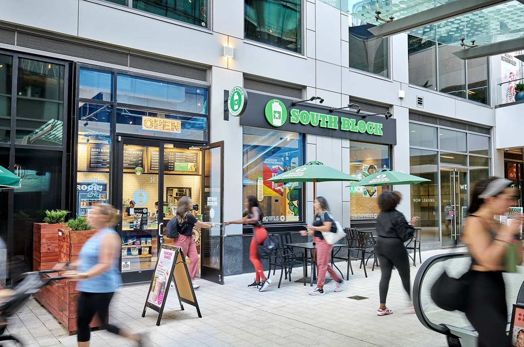A group of people are walking in front of a store with a green awning.