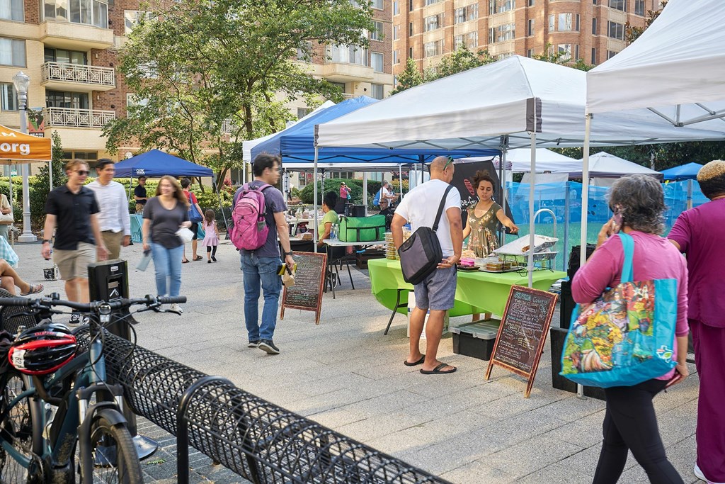 A busy outdoor market with people walking around and bicycles parked on the side.
