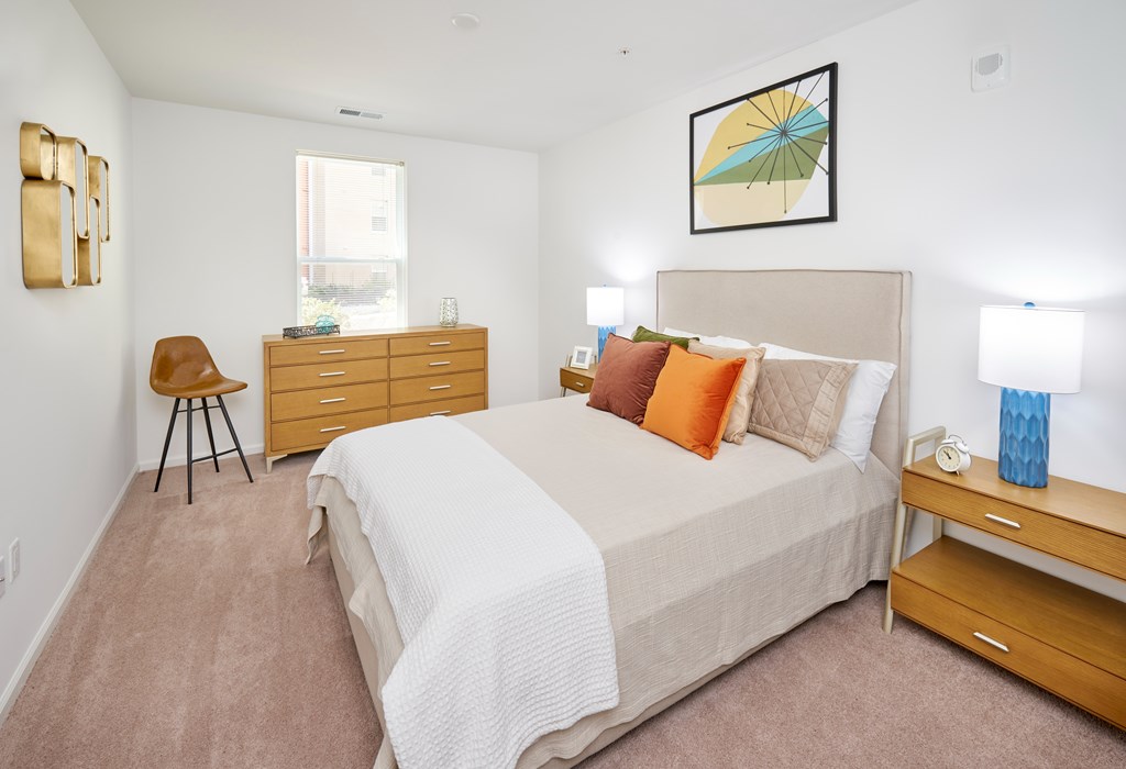 A bedroom with a bed, nightstand, chair, and a painting on the wall.