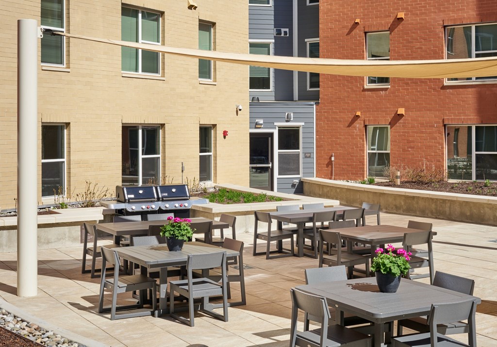 A patio with grey tables and chairs and a yellow awning.