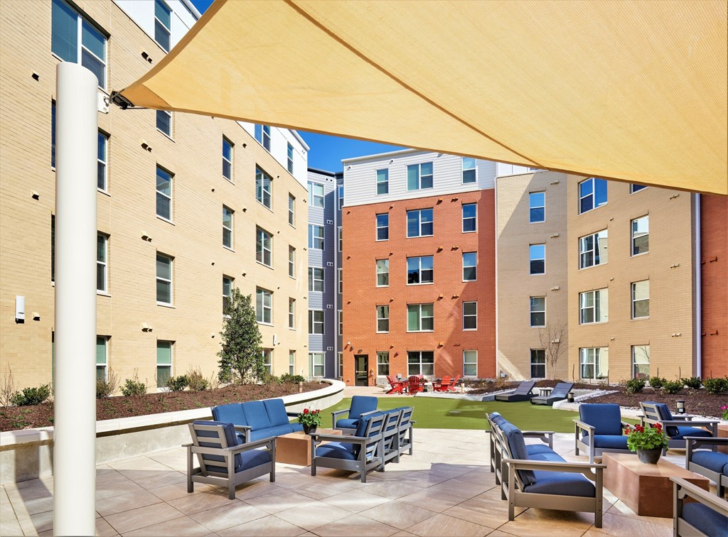 A patio with chairs and a table is shaded by a yellow canopy.