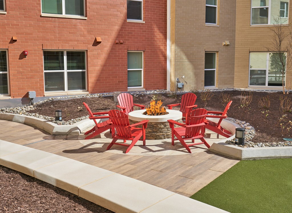 A patio with red chairs and a fire pit.