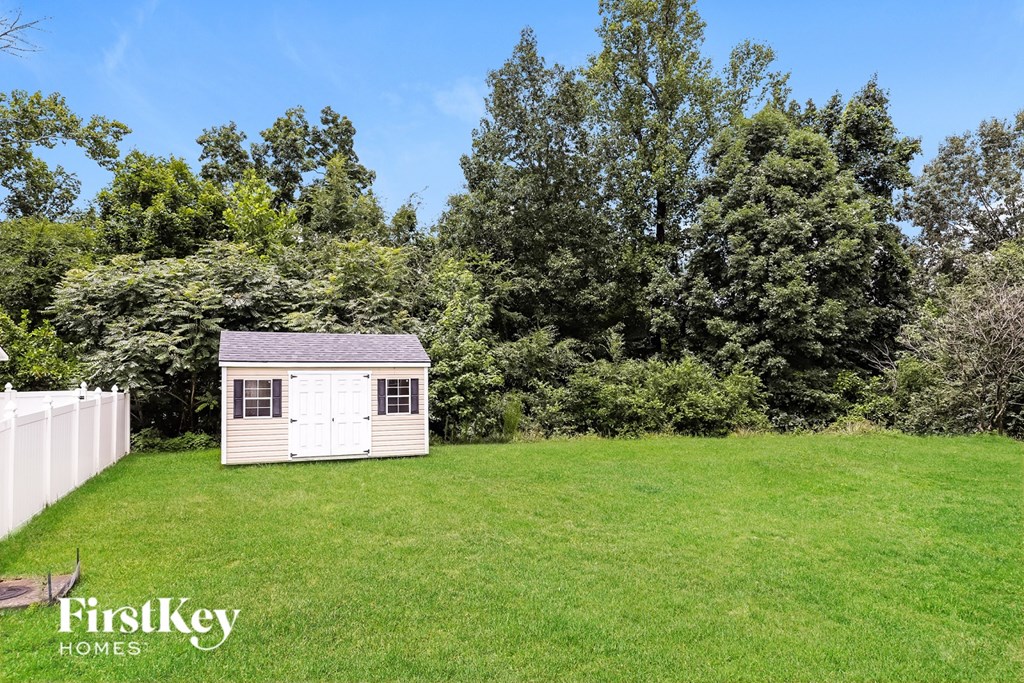A small white shed sits in a grassy field with trees in the background.