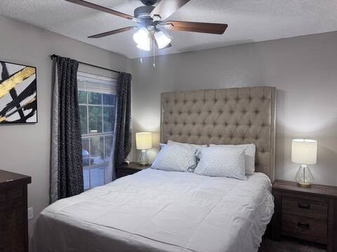 A bedroom with a large bed, a ceiling fan, and two lamps.