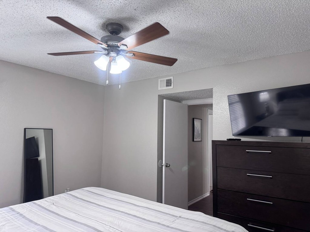A bedroom with a bed, dresser, and a ceiling fan.