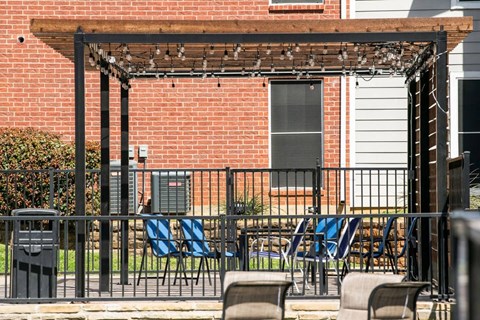 A patio with a pergola and chairs is in front of a brick building.