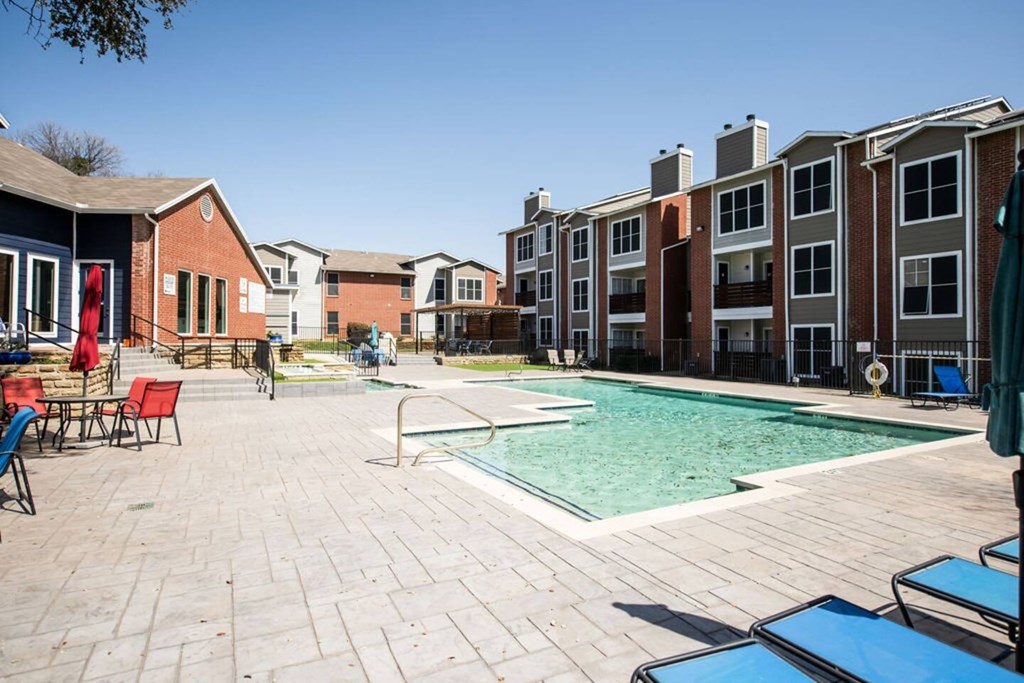 A swimming pool surrounded by a brick patio and chairs.